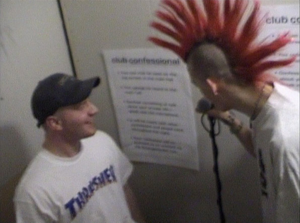 punk with red spiky hair speaks, friend looks on
